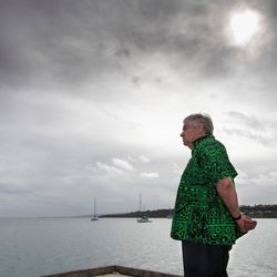 Guterres trägt ein grünes, gemustertes Hemd und blickt auf eine Meeresbucht, der Himmel ist bewölkt.