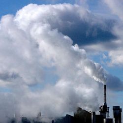Schornsteine einer Fabrikanlage stoßen dunkle Abgaswolken aus