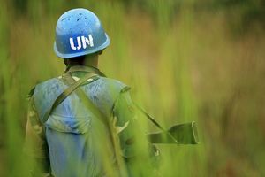 Ein Blauhelmsoldat der UN mit Gewehr in einem Feld.