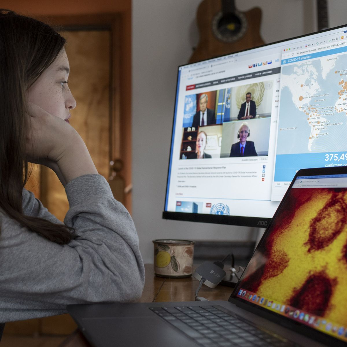 Mädchen vor zwei Computerbildschirmen, die eine Grafik des Corono-Virus und die Website des Humanitären Notprogramms anzeigen