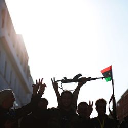 Eine Silhouette von Menschenmengen, die Gewehre und libysche Flaggen hochhalten.