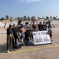Eine kleine Gruppe von Demonstrierenden steht auf einem leeren Platz eng beisammen. Sie halten ein Plakat mit folgender Aufschrift vor sich: Don't be scared of Climate Justice.