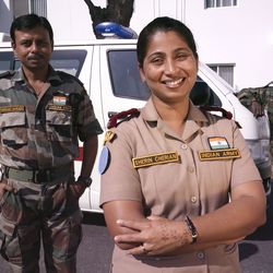 Eine Frau in Armeeuniform steht vor einem Krankenwagen. Im Hintergrund sind zwei männliche Kollegen zu sehen.