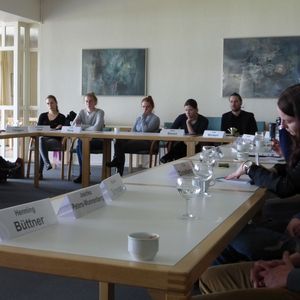 Eine Gruppe von Menschen sitzt in einem Seminarraum um mehrere Tische herum