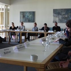 Eine Gruppe von Menschen sitzt in einem Seminarraum um mehrere Tische herum