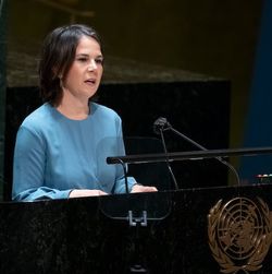Eine Frau in blauem Kleid spricht auf einem Rehdnerinnenpult in ein Mikrofon, an dem das UN-Logo angebracht ist.