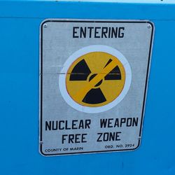 An einer blauen Wand hängt ein Schild mit einem durchgestrichenen Atomsymbol, darunter steht: Nuclear Weapon Free Zone