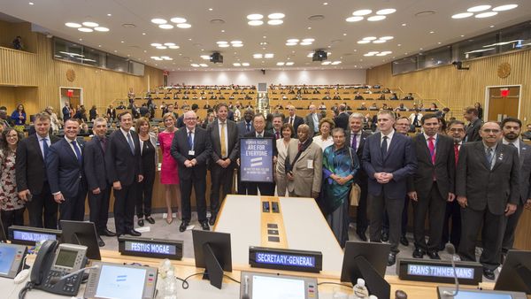 In einem großen holzvertäfelten Raum steht eine Menge an Menschen in einer Reihe nebeneinander. In der Mitte steht der ehemalige Generalsekretär Ban Ki-Moon. Fast alle lächeln freundlich in die Kamera.