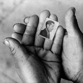 In seinen kleinen, herben Händen hält eine Person ein kleines Foto eines Mannes
