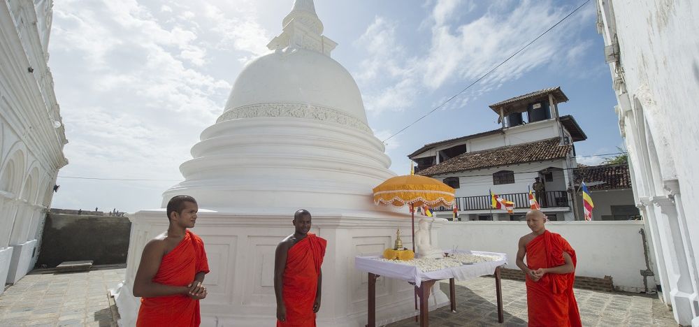 Buddhistische Mönche neben einem weißen buddhistischen Tempel gekleidet in traditioneller orangefarbener Bekleidung.