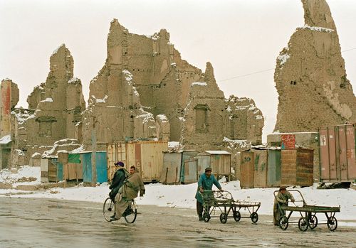 Einige afghanische Menschen vor den Ruinen zerstörter Häuser.