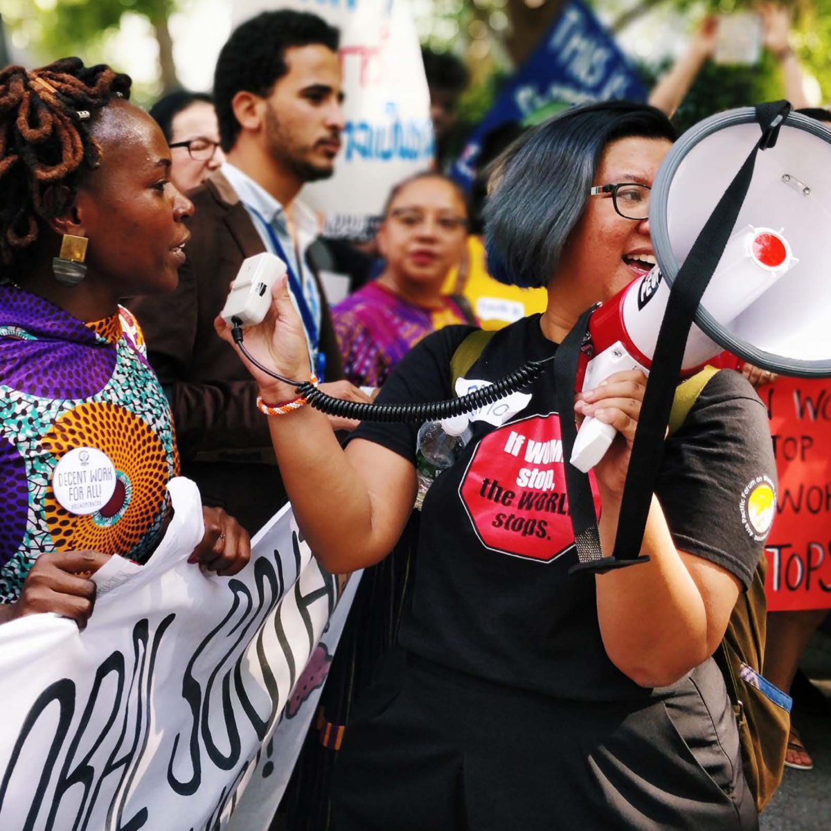 Mehrere Frauen demonstrieren, eine Frau hat ein Megafon in der Hand, eine andere trägt ein Transparent.