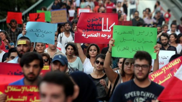 Eine Demonstration in Beirut. Es sind viele Menschen auf der Straße zu sehen die bunte, arabischsprachige Pappplakate in die Höhe über ihre Köpfe halten.