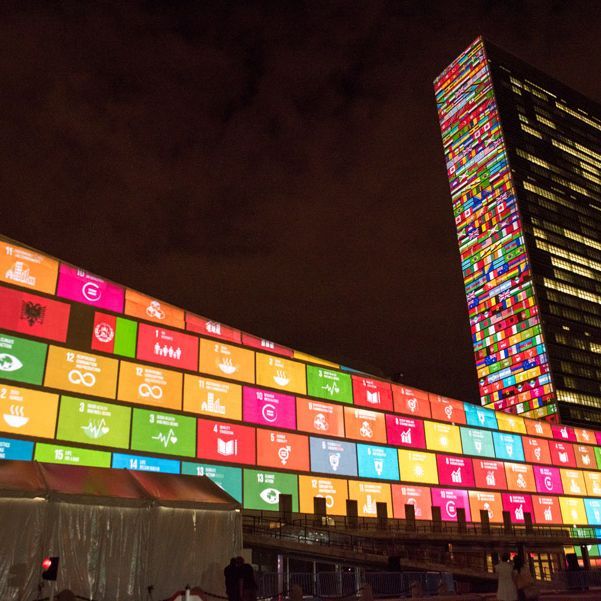 Auf dem Bild ist das UN-Hauptgebäude in New York bei Nacht zu sehen. Beleuchtet wird es mit allen SDG-Icons.