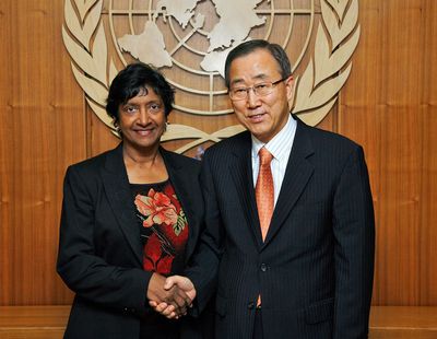 Navi Pillay und Ban Ki-moon schütteln sich die Hand und lächeln dabei freundlich in die Kamera, im Hintergrund sieht man das Logo der UN