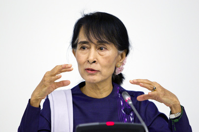 Aung San Suu Kyi sitzt vor einem Mikrofon und gestikuliert.