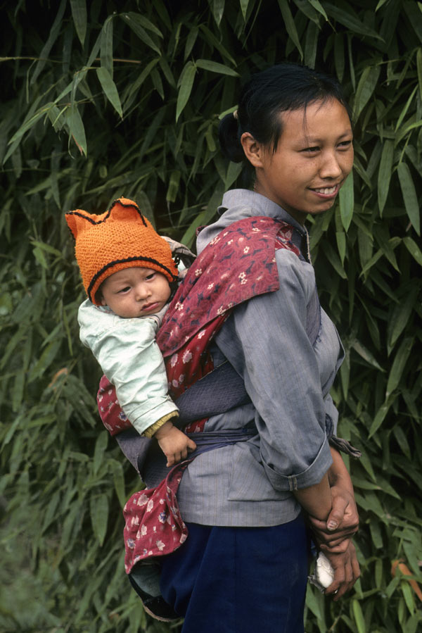 Eine lächelnde Mutter trägt ihr Kind hinter sich in einem Tragetuch