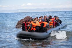 Übervolles Schlauchboot mit Flüchtlingen auf dem Meer vor der griechischen Küste. Die Menschen, Frauen und Männer, tragen Rettungswesten.